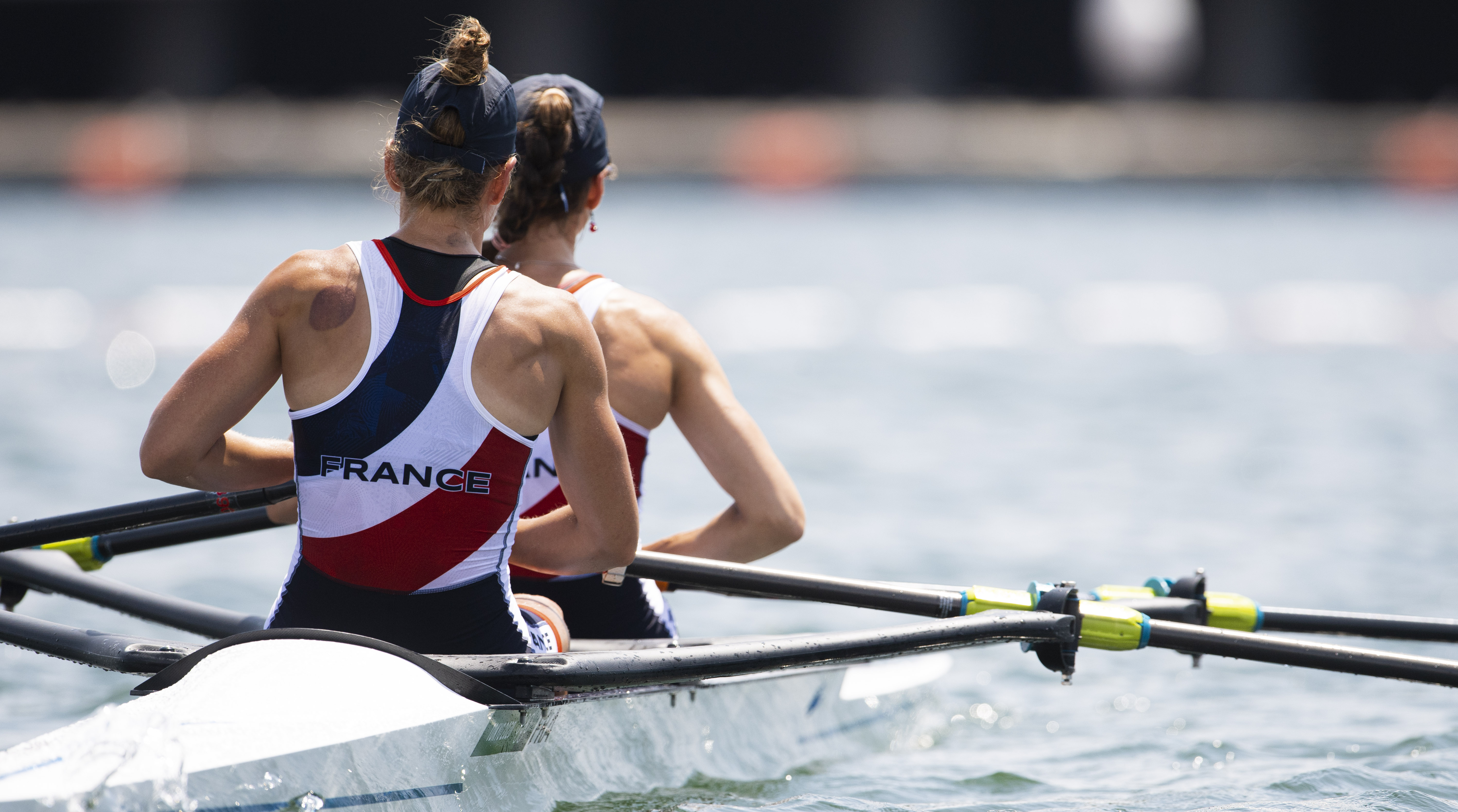 Deux rameuses françaises vues de dos, à bord d'un bateau d'aviron sur l'eau.