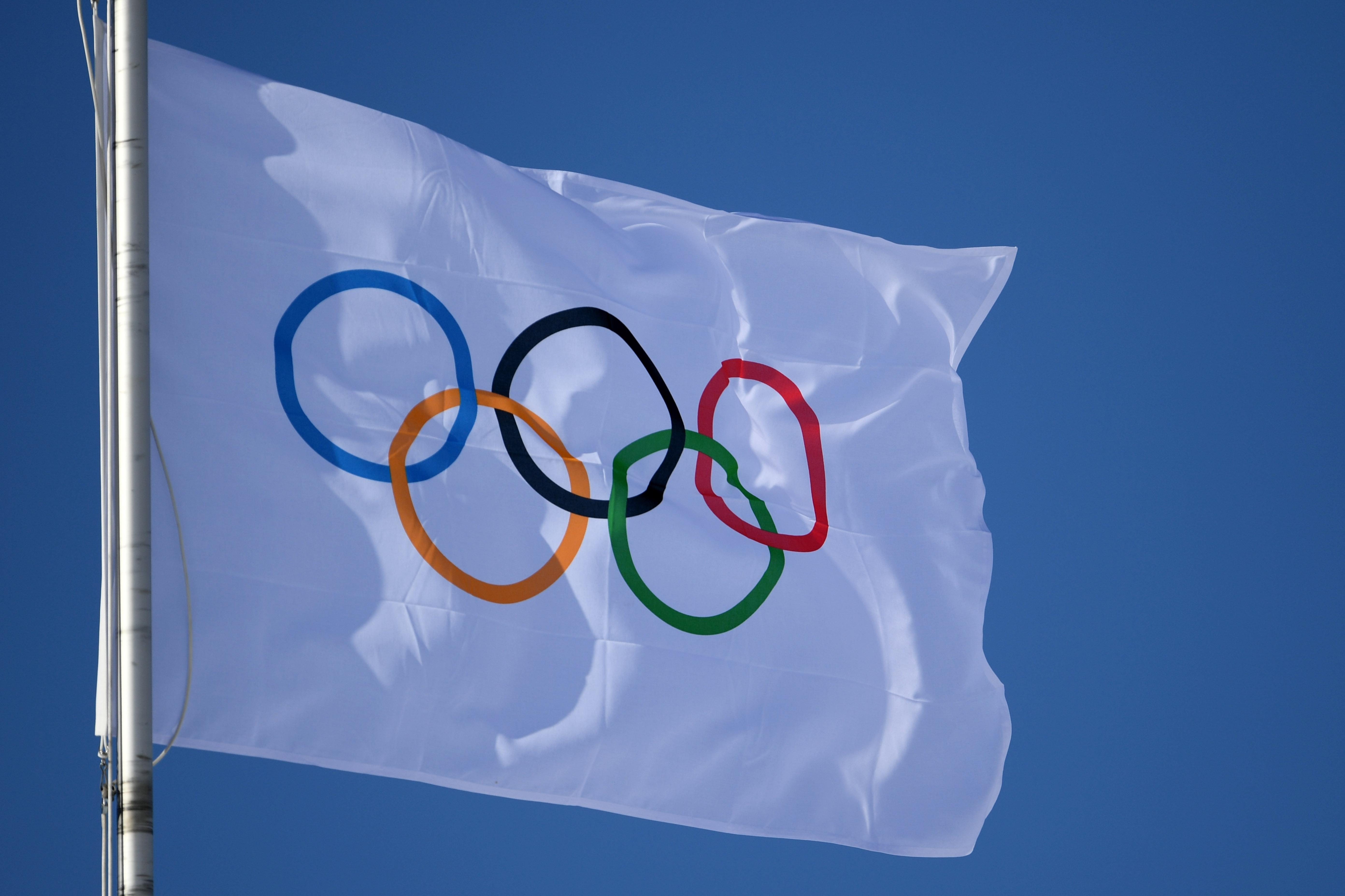 Drapeau olympique blanc flottant dans le ciel bleu, avec les cinq anneaux olympiques entrelacés.