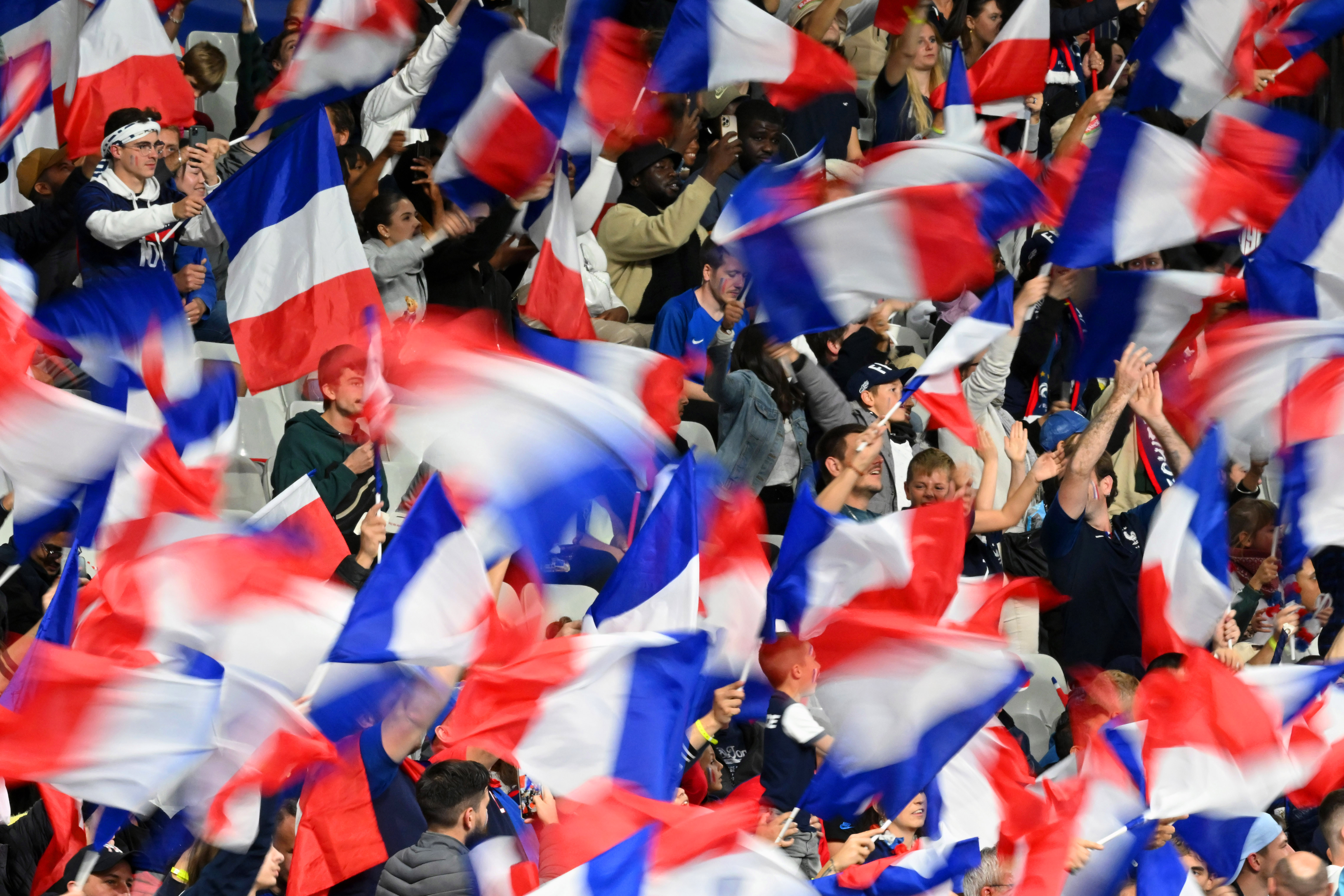 Foule de supporters français agitant des drapeaux tricolores dans les tribunes d'une compétition sportive.