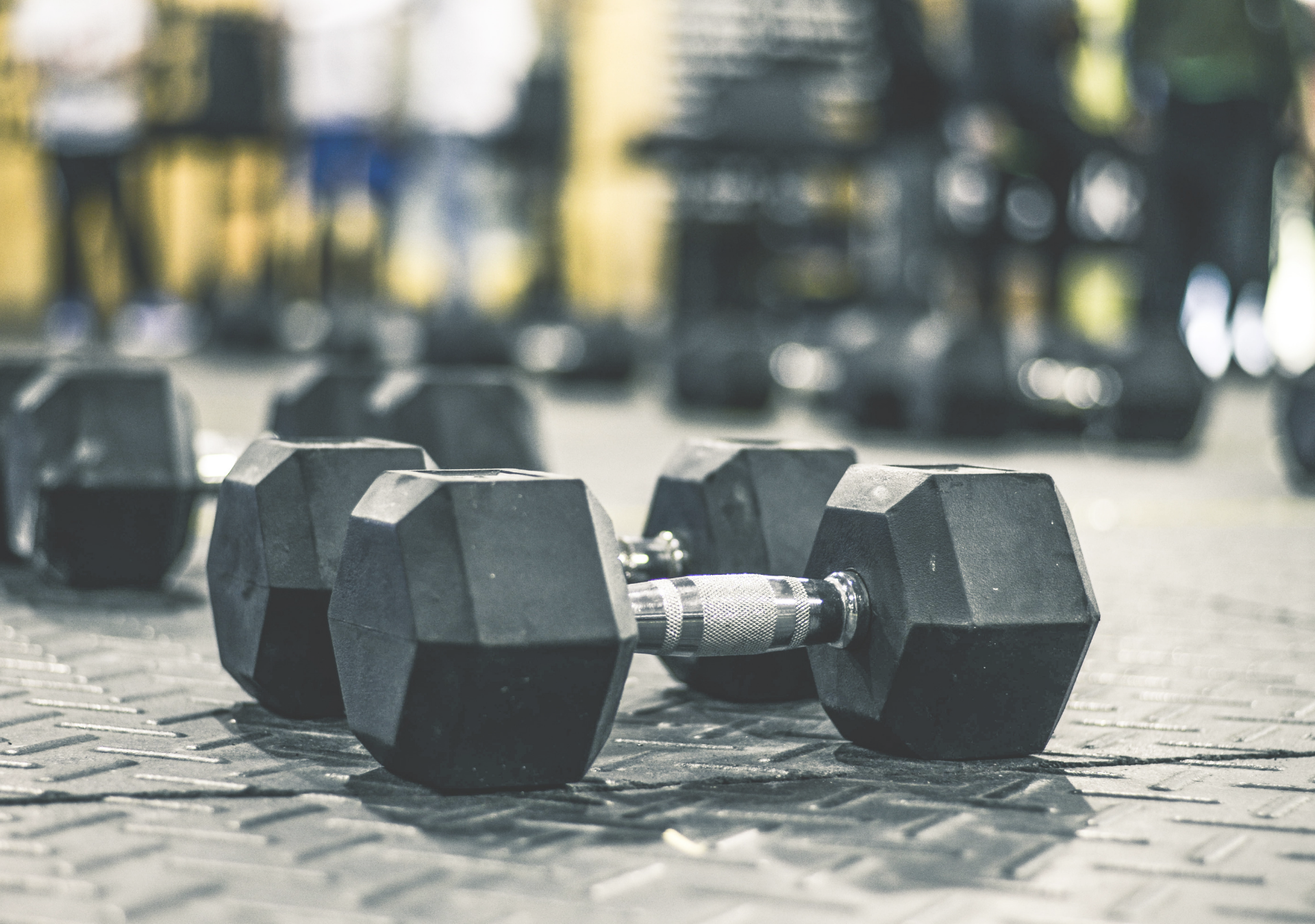 Haltères de musculation posés sur le sol d’une salle de sport, avec d’autres équipements sportifs flous en arrière-plan.